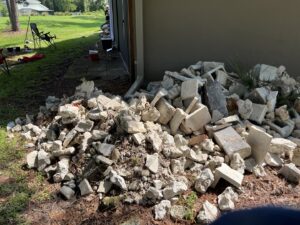 A large pile of concrete and cinder block debris next to a house, ready for removal by DUMP 4 U Hauling in Jacksonville, FL