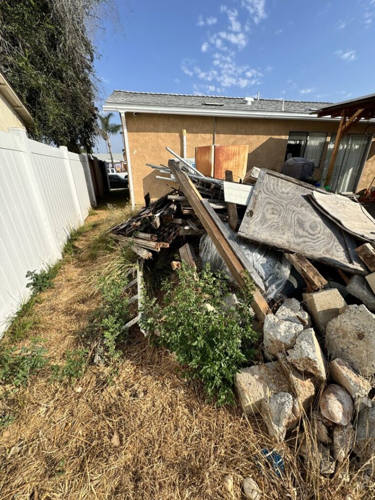 A large pile of construction debris, wood, and concrete junk in a side yard, ready for removal by Johan's Junk Removal in San Diego, CA.