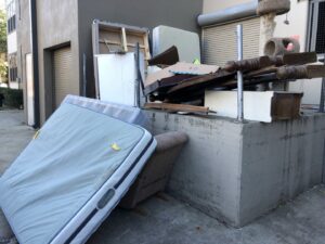 A large pile of discarded mattresses, furniture, and general debris accumulated outside a building, awaiting removal by Perez Junk Removal in Anaheim, CA.