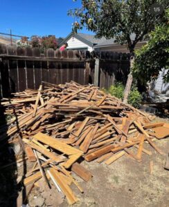 A large pile of wood debris in a backyard, indicating a cleanout job for Stars Junk Removal in San Jose, CA