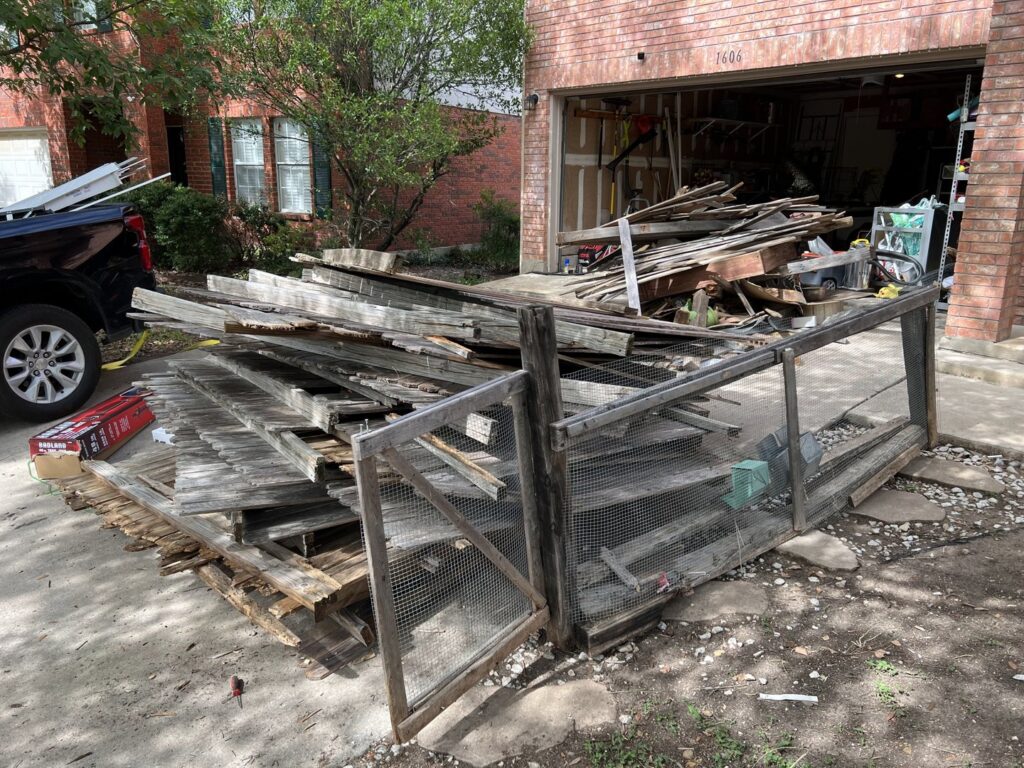 A large pile of wood and fence debris in front of a garage, ready for removal by Texas Strong Hauling and Junk Removal in San Antonio, TX.