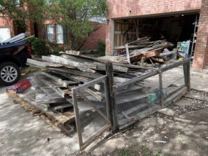 A large pile of wood and fence debris in front of a garage, ready for removal by Texas Strong Hauling and Junk Removal in San Antonio, TX.