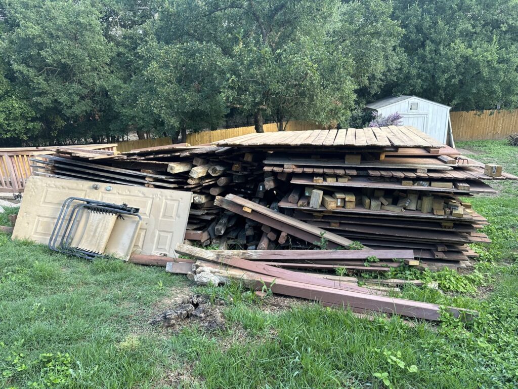 A large pile of wood and construction debris in a backyard, ready for removal by 2 Bald Guys Hauling & Junk Removal in San Antonio, TX.