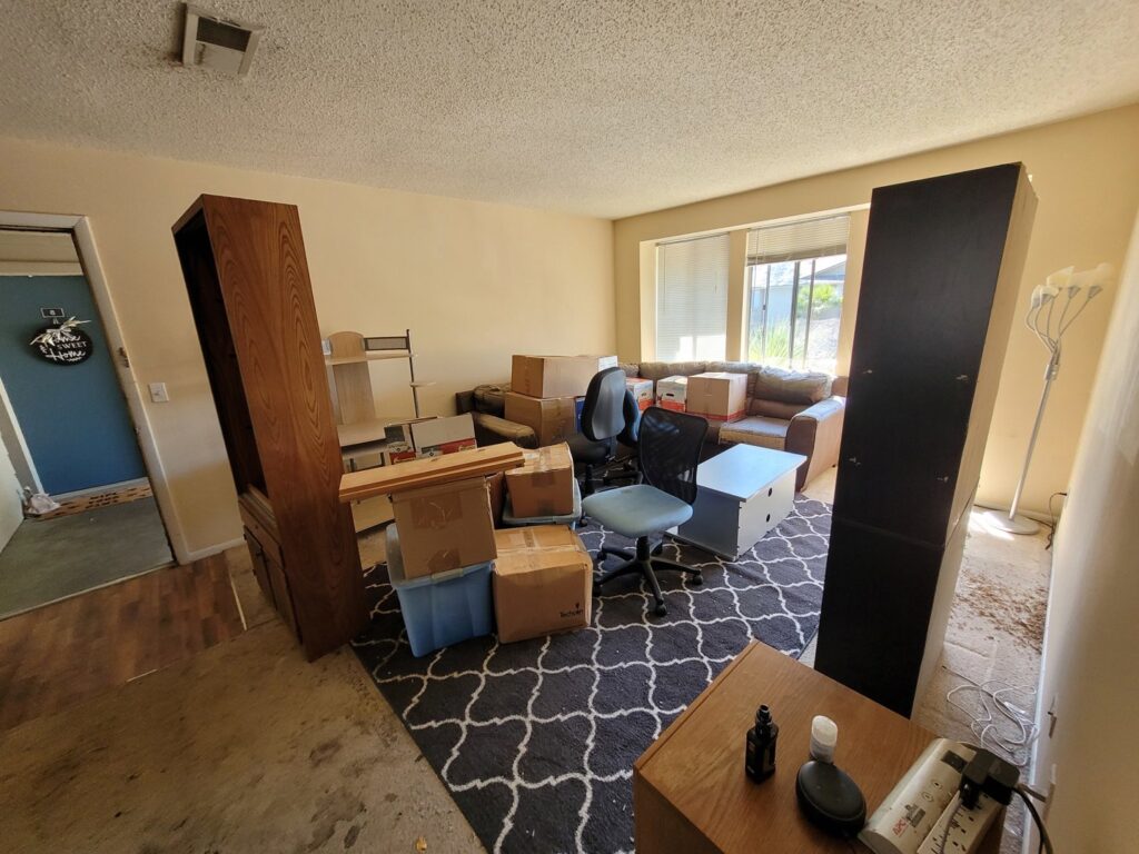 A living room filled with moving boxes, furniture, and an office chair, indicating a residential cleanout service by Jacksonville Hauling & Junk Removal in Jacksonville, FL.