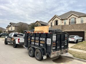 A Hud's Haul Away Junk Removal & Demolition trailer partially loaded with debris on a residential street in Fort Worth, TX.