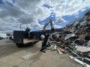 A Haul Away Any Day team member loading an elliptical machine next to a large pile of scrap metal for removal in San Diego, CA.