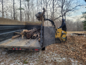 A worker loading logs and branches into a dump trailer using a skid steer for junk removal by Schott Services in Indianapolis, IN.