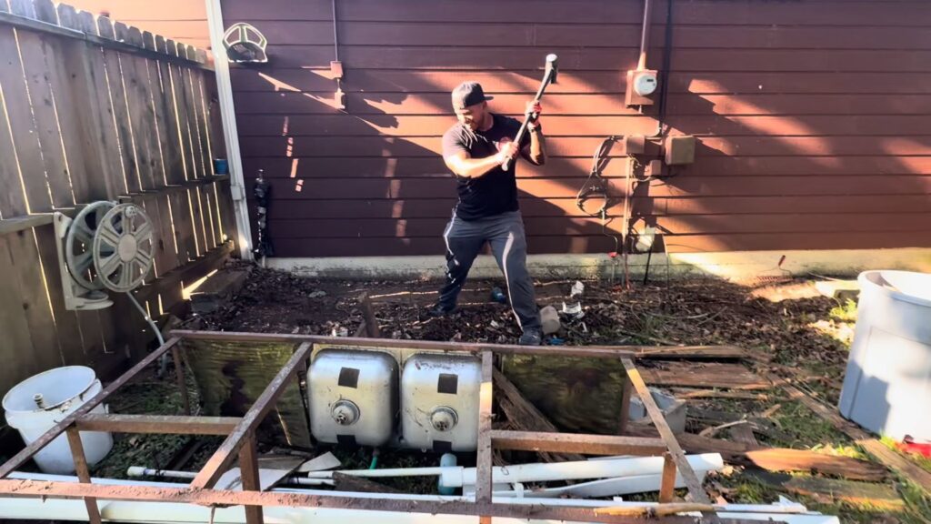 A Clutch City Junk Removal team member demolishing an old outdoor sink structure in a backyard in Tomball, TX.