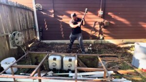 A Clutch City Junk Removal team member demolishing an old outdoor sink structure in a backyard in Tomball, TX.