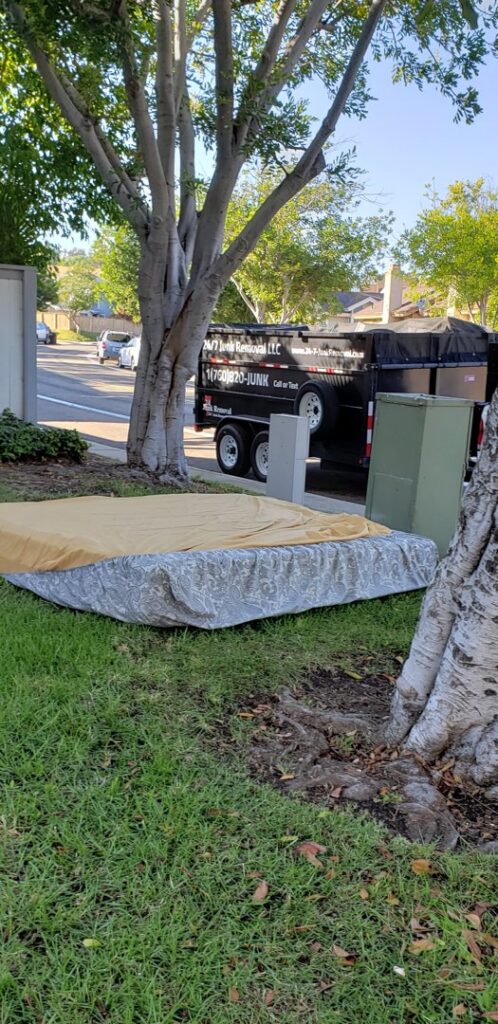 A mattress placed on a lawn for pickup, with a 24/7 Junk Removal trailer in the background in Rolling Hills Estates, CA.
