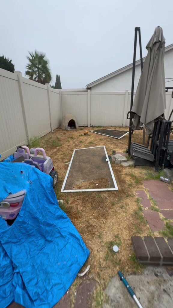 A messy backyard with a blue tarp, children's toys, and a screen door, ready for a cleanout by Johan's Junk Removal in San Diego, CA.