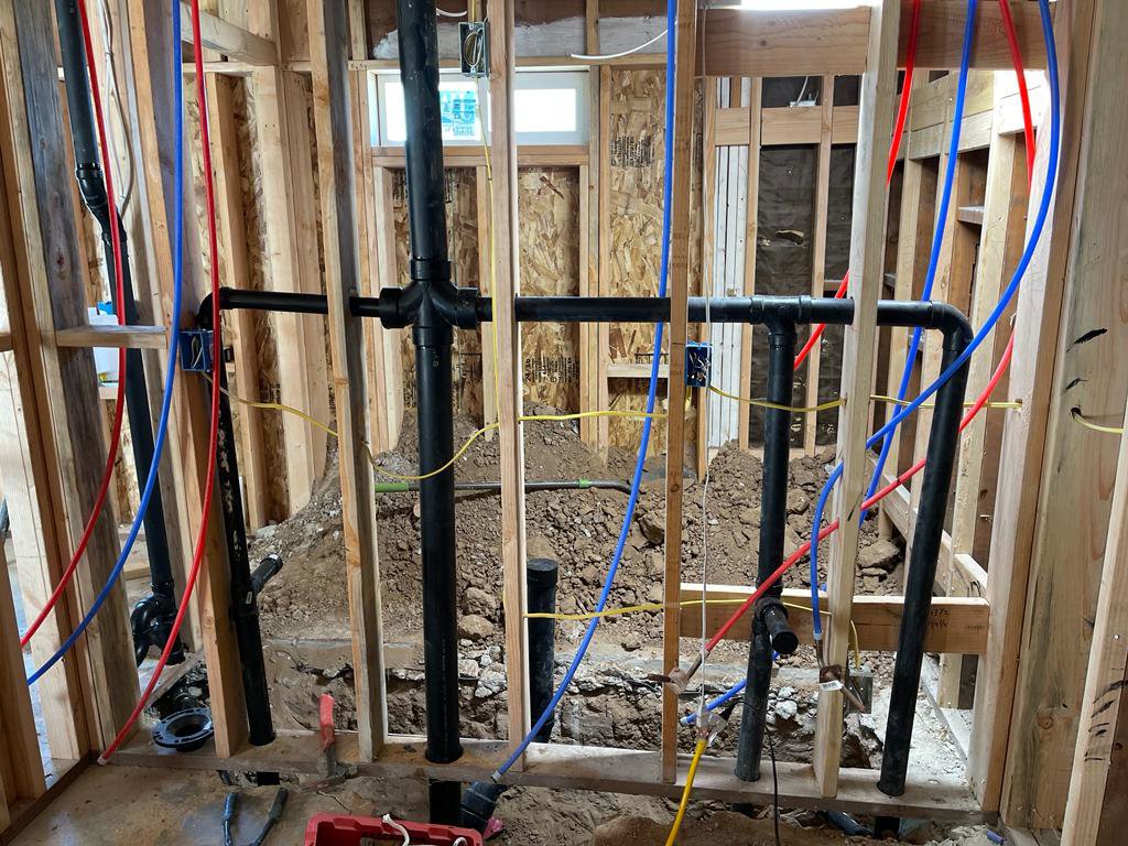 New plumbing pipes, including drainage and PEX supply lines, installed in a framed wall during construction by Plumbing Services Inc. in San Diego, CA.