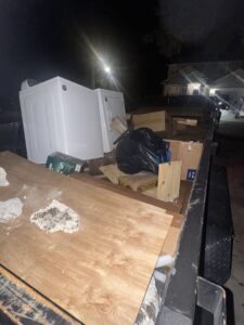 A dump trailer loaded with appliances and various junk at night, indicating a completed junk removal job by Jax Junkies Removal LLC in Jacksonville, FL