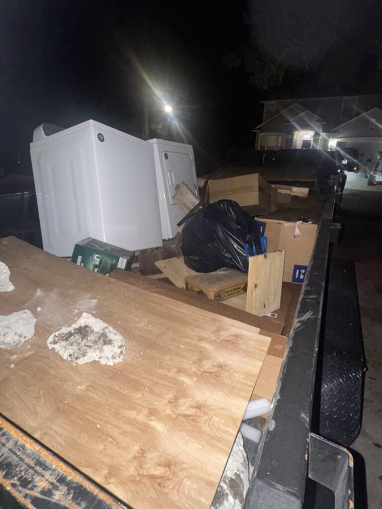 A dump trailer loaded with appliances and various junk at night, indicating a completed junk removal job by Jax Junkies Removal LLC in Jacksonville, FL