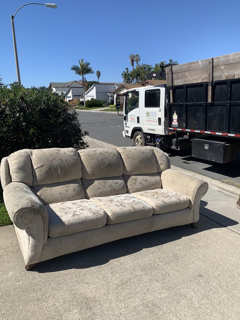 An old sofa placed on the sidewalk next to a Fred's Junk Removal truck in Chula Vista, CA.