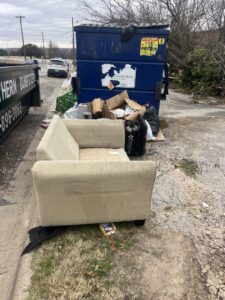 An old sofa and various junk items piled next to dumpsters, awaiting removal by NTX Haul Away Junk Removal in Fort Worth, TX.