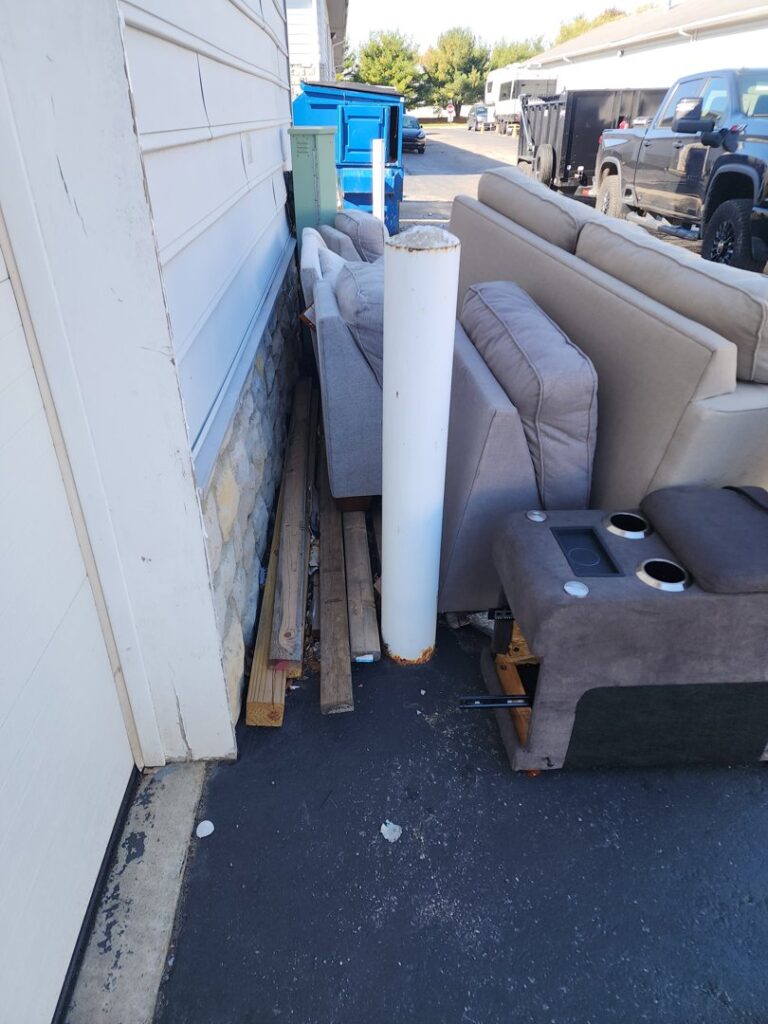 Old sofas and wooden planks piled against a house, awaiting removal by Master Junkers in Powell, OH.
