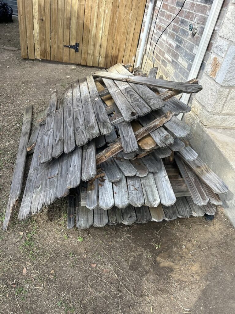 A pile of old, weathered wooden fence panels stacked for removal by Texas Junk Masters in Fort Worth, TX.