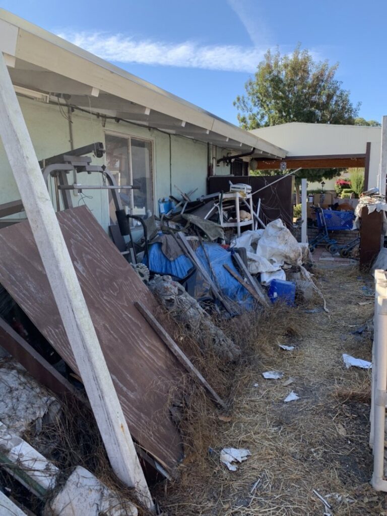 A large pile of outdoor debris, including wood, tarps, and exercise equipment, next to a house for removal by Zen Junk in San Jose, CA.