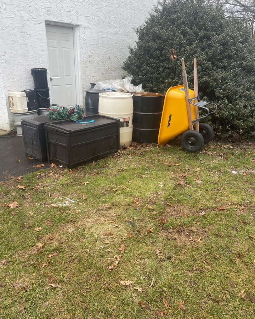 An outdoor pile of various items including barrels, a wheelbarrow, and storage bins, ready for removal by JPC Junk Removal & Demolition in Philadelphia, PA.