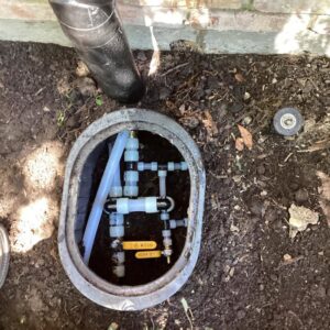 An outdoor plumbing manifold system with pipes and valves in an access box, serviced by Tribeca Plumbing in Dallas, TX.