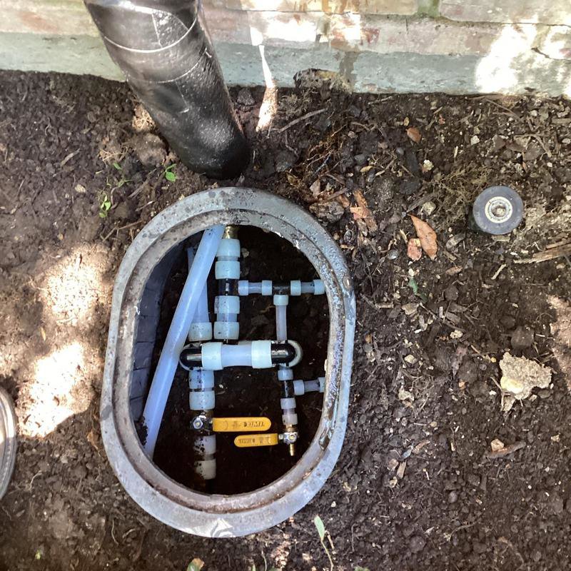 An outdoor plumbing manifold system with pipes and valves in an access box, serviced by Tribeca Plumbing in Dallas, TX.