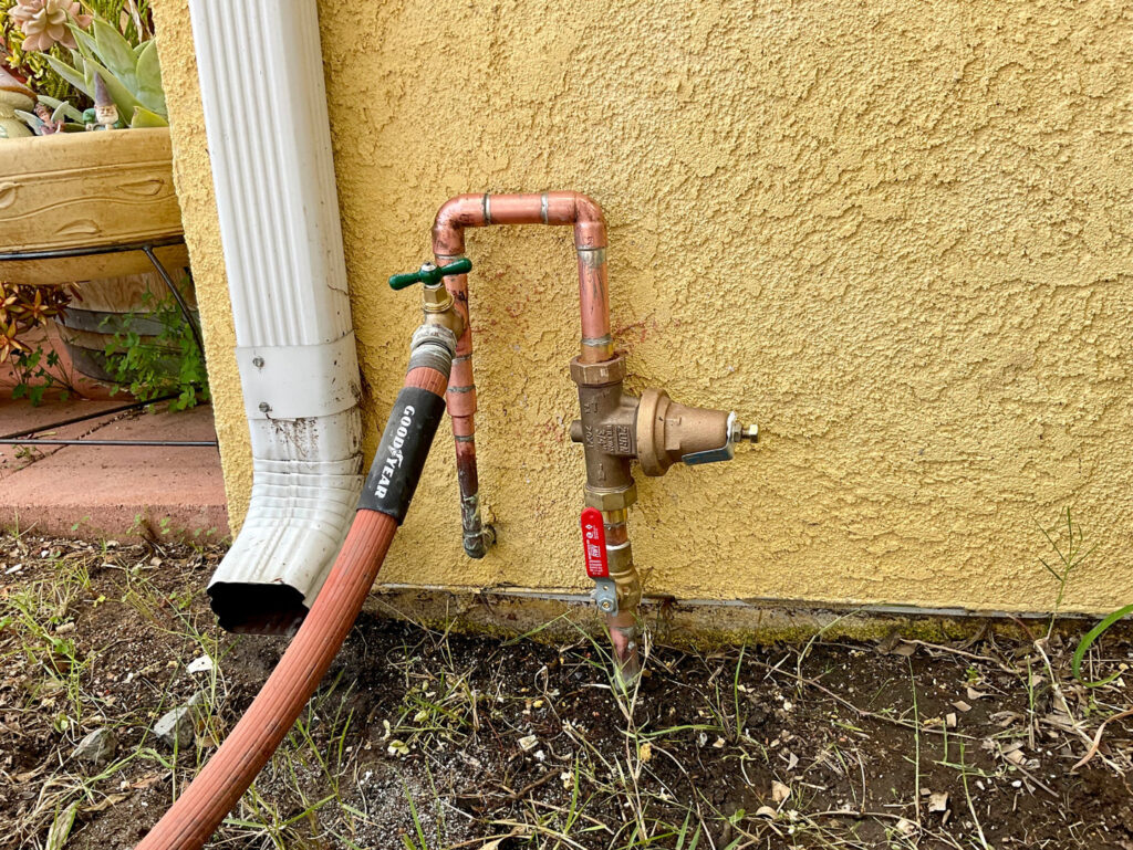 Outdoor plumbing showing a pressure regulator and copper piping installed by JG Water Heaters, Filtration and Plumbing in San Diego, CA