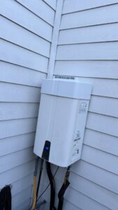 An outdoor tankless water heater installed on the corner of a house by Economy Plumbing Services in Austin, TX