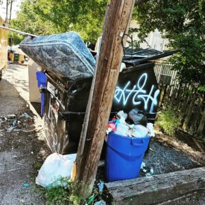 An overflowing dumpster and trash cans with a mattress, indicating a site ready for junk removal by Junk Out Boyz LLC in Austin, TX.