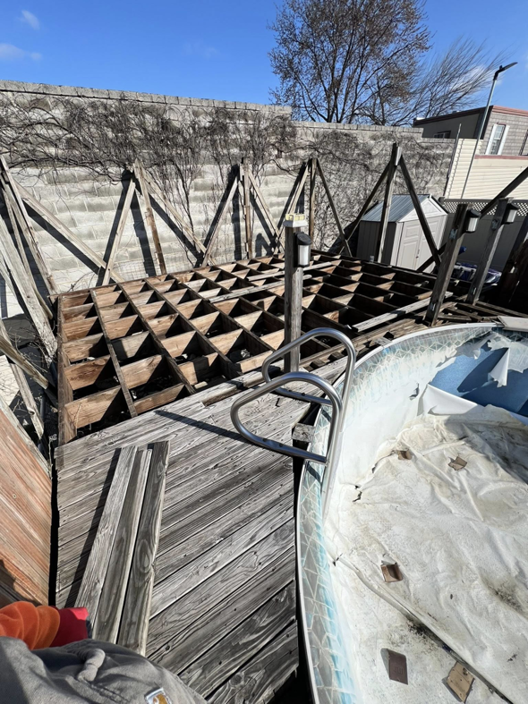 A partially dismantled wooden deck frame next to an old pool during a cleanout job by Affordable Cleanouts LLC in Philadelphia, PA.