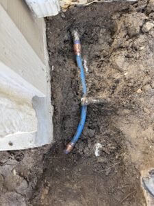 A blue PEX water line connected to copper piping in a trench, indicating a repair by The Bearded Plumber in San Antonio, TX.