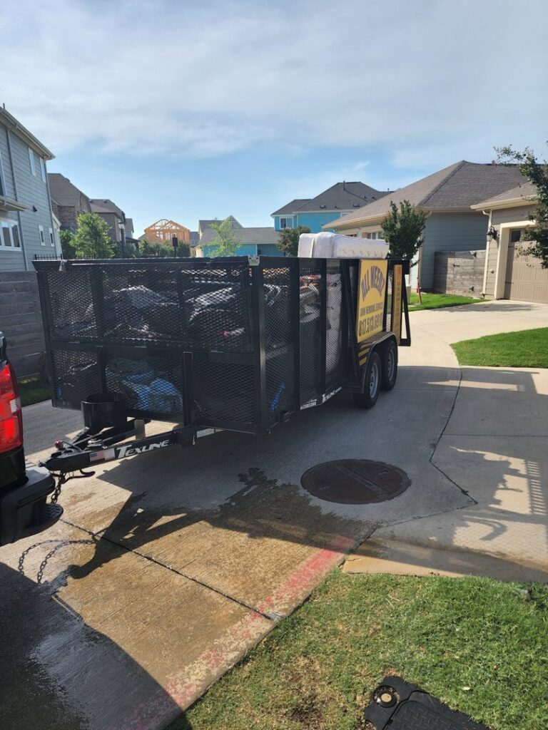 A large pile of various junk items on a sidewalk next to a trailer from All Needz Junk Removal & Hauling Service in Dallas, TX, ready for pickup.