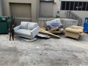 A pile of discarded sofas, chairs, and wood debris outside a building, ready for removal by Perez Junk Removal in Anaheim, CA.