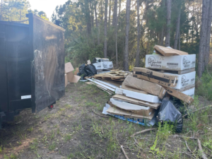 A large pile of cardboard, wood, and trash bags next to a dump trailer, ready for removal by Jax Junkies Removal LLC in Jacksonville, FL