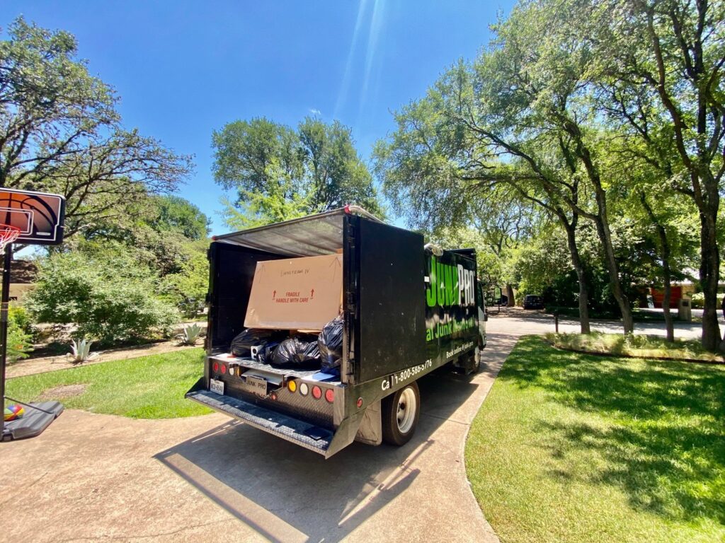 A large pile of various junk items, including boxes and carpet, on a residential driveway in Austin, TX, ready for removal.