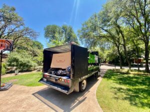 A large pile of various junk items, including boxes and carpet, on a residential driveway in Austin, TX, ready for removal.