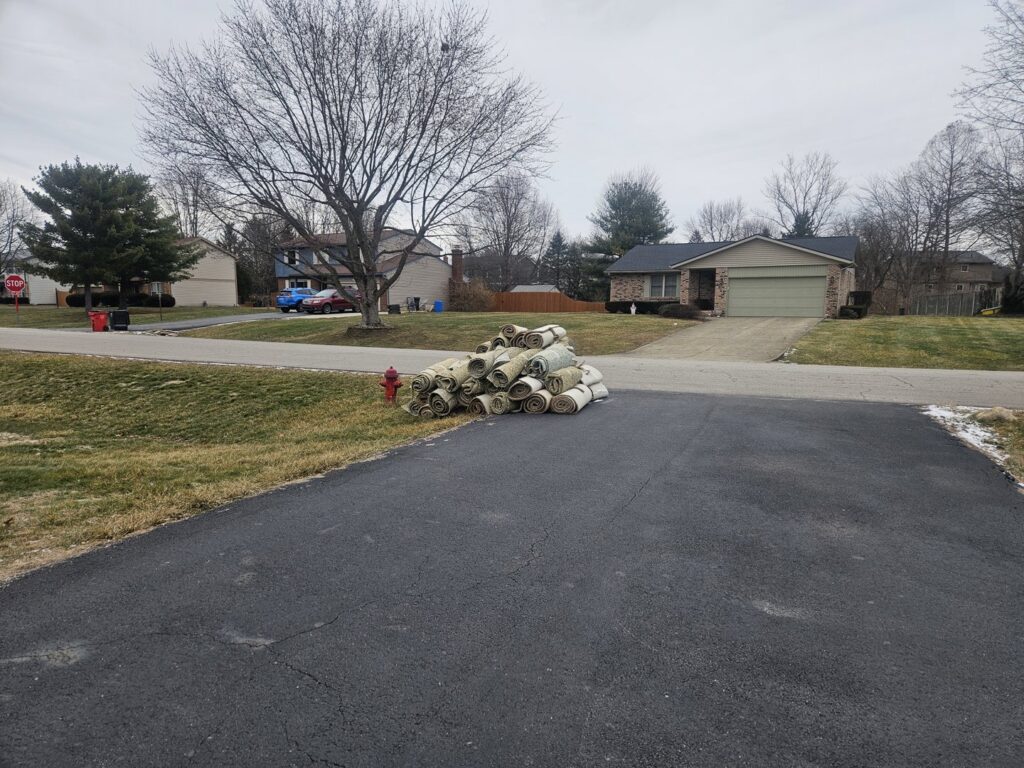A large pile of rolled-up old carpets on a driveway, ready for junk removal by Junk Fellas LLC in Columbus, OH.