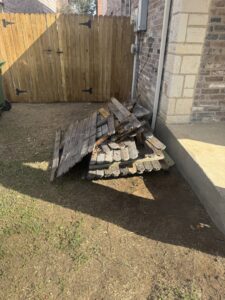 A pile of old wooden fence panels stacked next to a house for removal by Texas Junk Masters in Fort Worth, TX.