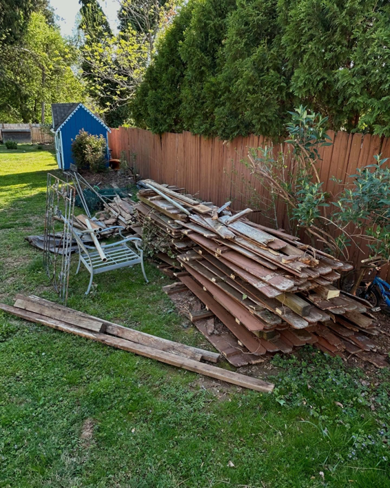 A large pile of old wooden fence panels and yard debris in a backyard, ready for junk removal by Nolen's Junk Removal in Feasterville-trevose, PA.