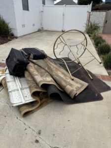 A pile of rugs, luggage, and a small table on a driveway for Fred's Junk Removal in Chula Vista, CA.