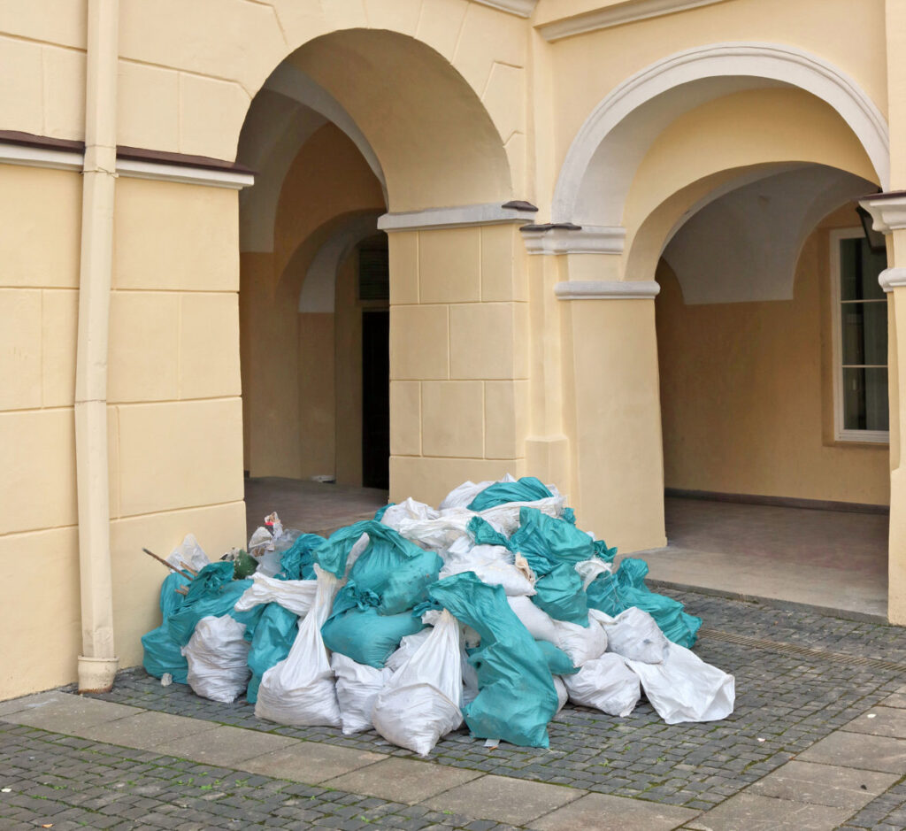 A pile of white and teal trash bags accumulated outside a building, awaiting waste removal by Zen Junk in San Jose, CA.