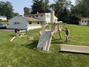Junk to Go workers dismantling an old wooden playset in a backyard for removal service in Philadelphia, PA.