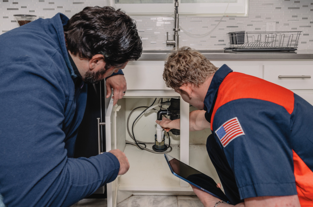 A Service Squad Plumbing technician and a customer inspecting pipes under a kitchen sink in Fort Worth, TX.