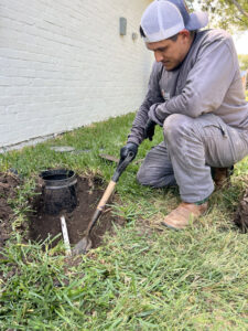 A Molberg Plumbing technician digging around an outdoor water meter access in Ft Worth, TX