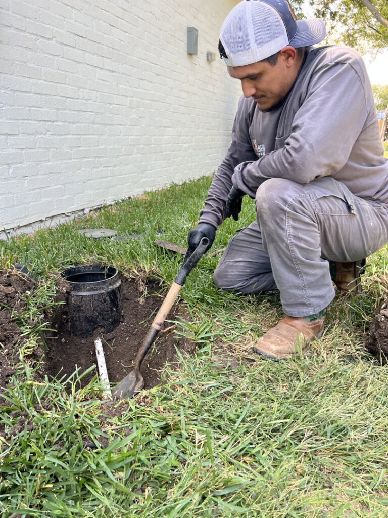 A Molberg Plumbing technician digging around an outdoor water meter access in Ft Worth, TX