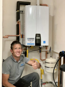 A plumber from JG Water Heaters, Filtration and Plumbing giving a thumbs-up next to a newly installed tankless water heater in San Diego, CA