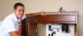 A plumber smiling next to sink pipes and a garbage disposal unit for Reliable Plumbing Services in Houston, TX