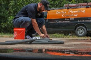 A plumber from Dallas Plumbing Company working on pipes and hoses on the ground in Dallas, TX.