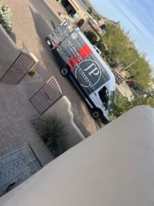 A plumber from JP Plumbing working under a sink with a flashlight, performing a repair or installation in Phoenix, AZ
