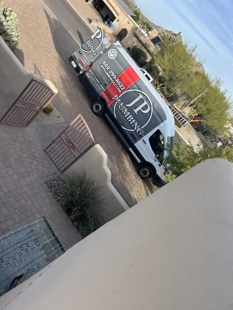 A plumber from JP Plumbing working under a sink with a flashlight, performing a repair or installation in Phoenix, AZ